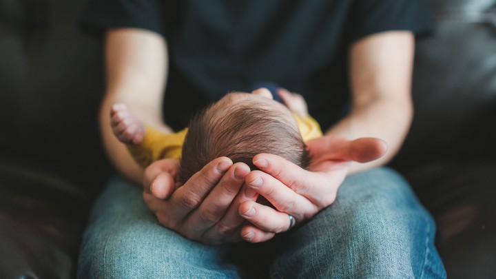 A baby lies on its back in a man's lap.
