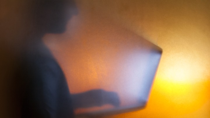 The silhouette of a man looking at a bright computer screen