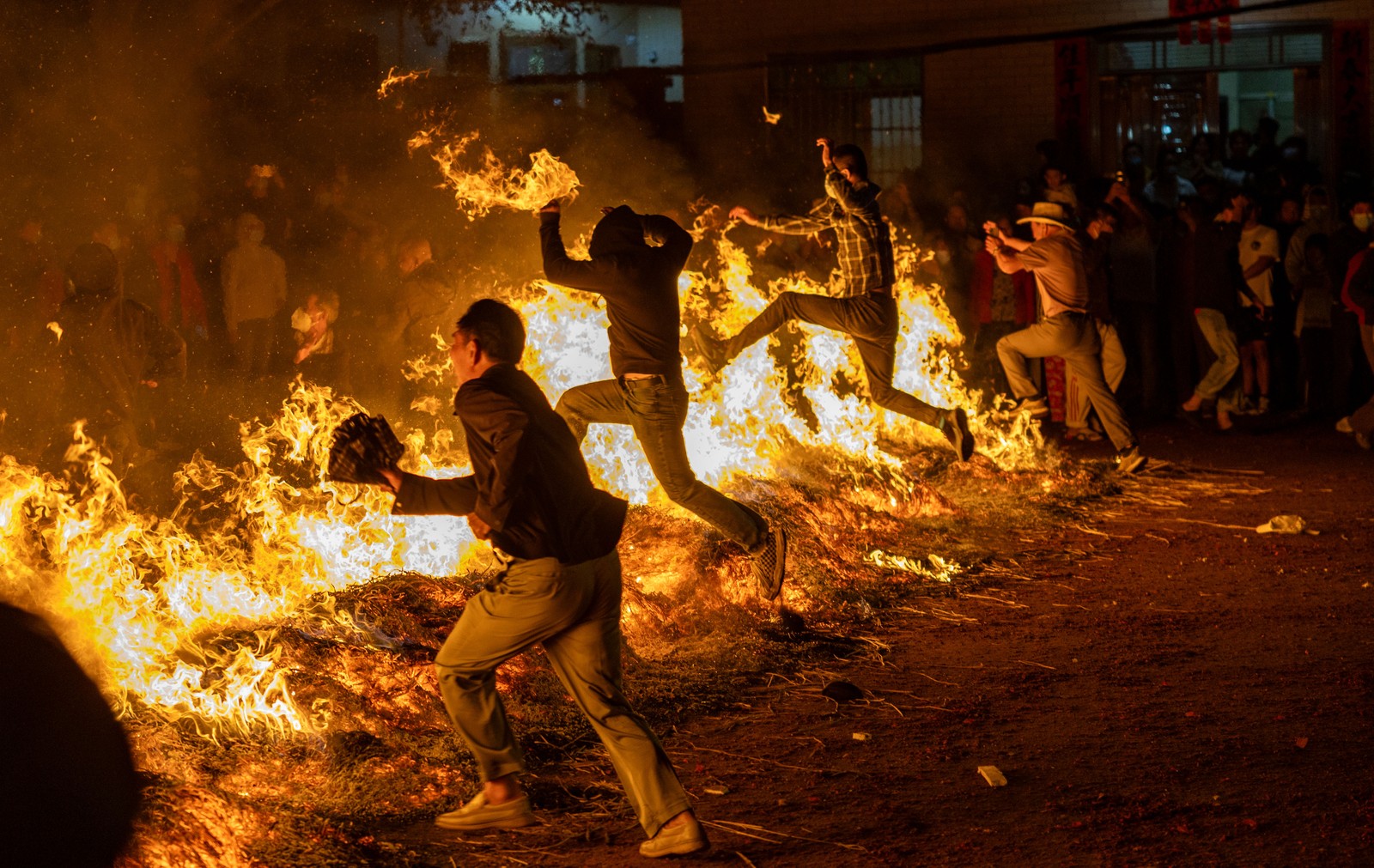 Several people jump through a bonfires to celebrate at a festival.