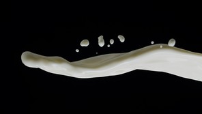 A stream of white liquid splashing onto a dark background from the right side of the image