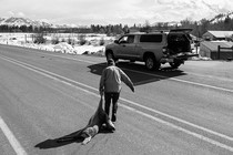 A man drags a dear carcass across a road to his car