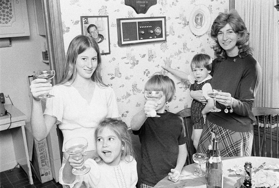 A mother and her four children stand beside a table holding up glasses and smiling for the camera.