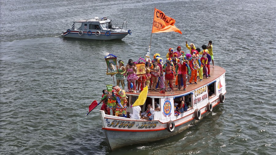 Costumed revelers stand atop a small boat in a river.