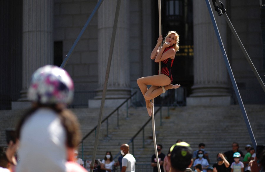 An acrobat climbs a rope on a street in front of an audience.