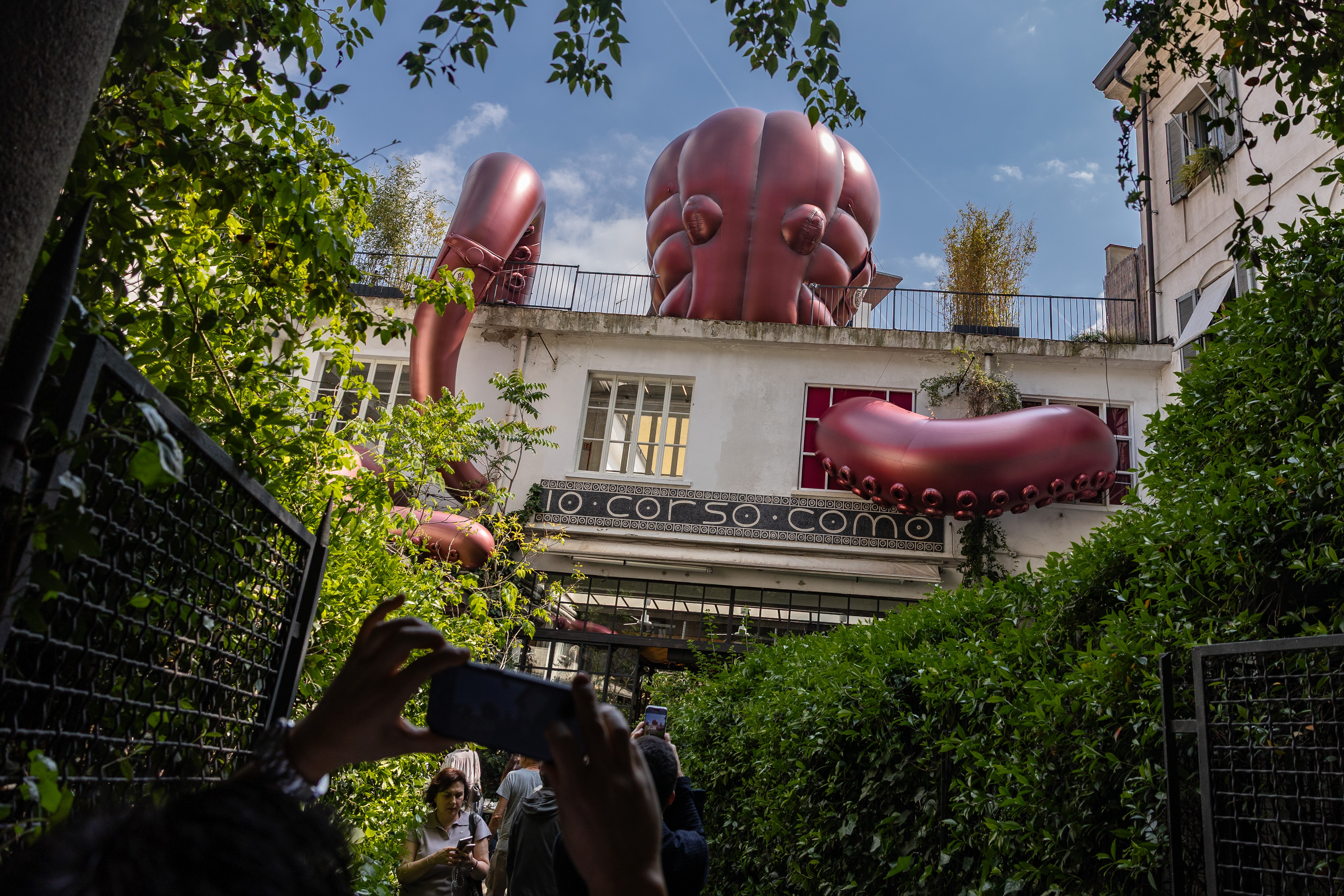 People take pictures of a giant inflatable octopus clinging to the façade of a building.