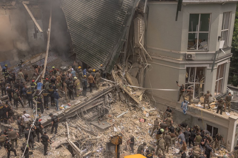 Many rescue workers stand atop and near rubble around a partially collapsed building.