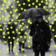 Photo of someone, masked, on the street with an umbrella; glowing dots overlaid like snow