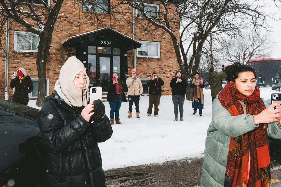A crowd of people film ICE agents and blow their whistles
