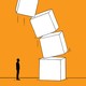 A small figure stands in front of a big stack of toppling boxes.
