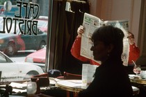 A man in a café holds up a newspaper to read it.