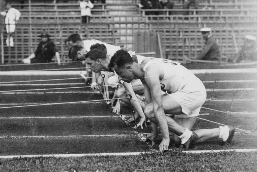 Runners kneel at a starting line, preparing to start a 100 meter race.