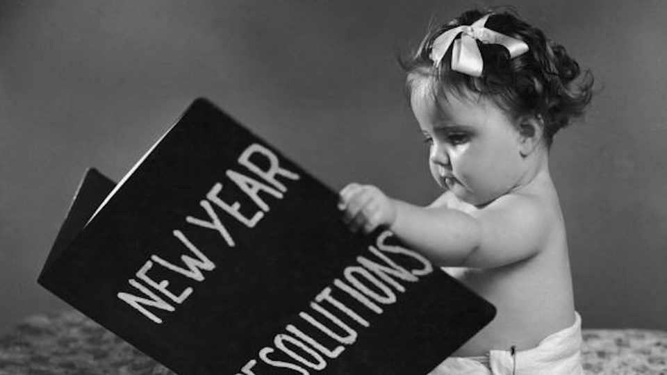 Circa 1955: A baby wearing diapers sits and holds a large book of New Year Resolutions.