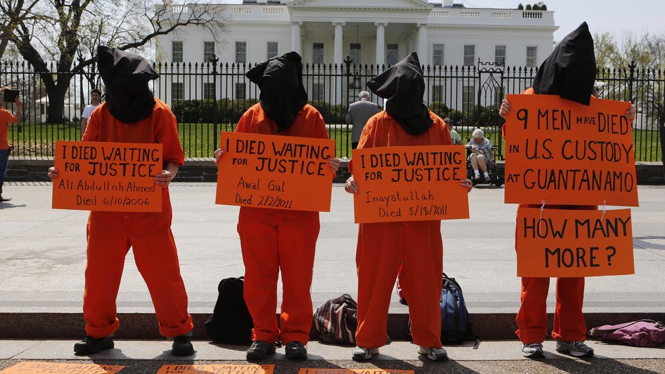 Four activists dressed up as Guantanamo Bay prisoners in front of the White House hold signs that accuse the U.S. administration of ignoring the deaths of prisoners waiting to be released from the U.S. prison in Cuba.