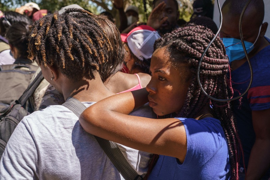A group of migrants stand together, listening to a news report.