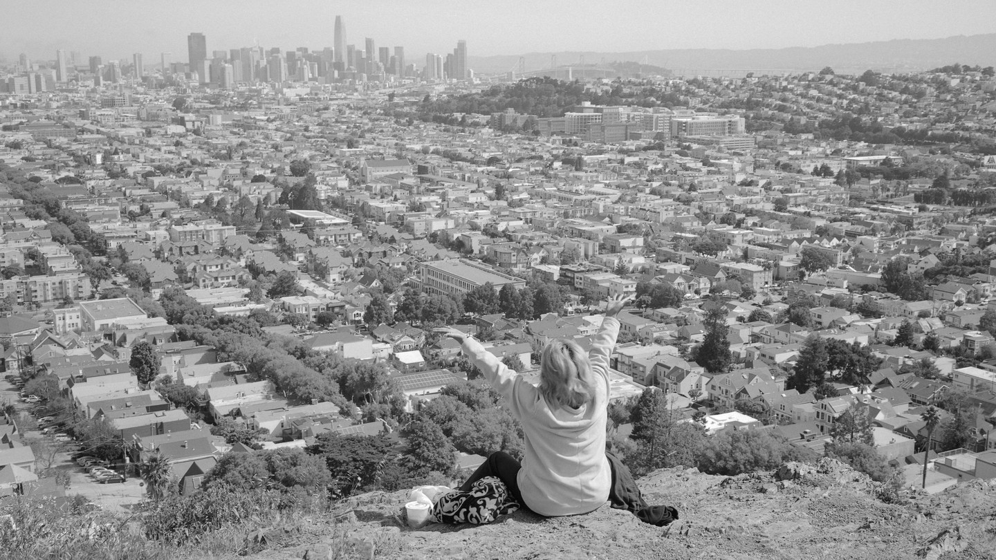 A black-and-white image of a  woman raising her hands overlooking the city of San Francisco