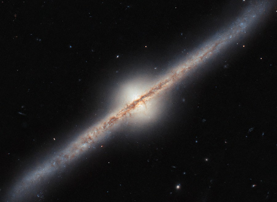 A spiral galaxy seen directly from the side, such that its disc looks like a narrow diagonal band across the image. A band of dark dust covers the disc in the center most of the way out to the ends, and the disc glows around that.