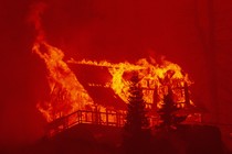 A view of a house in a forest, completely consumed by fire, at night