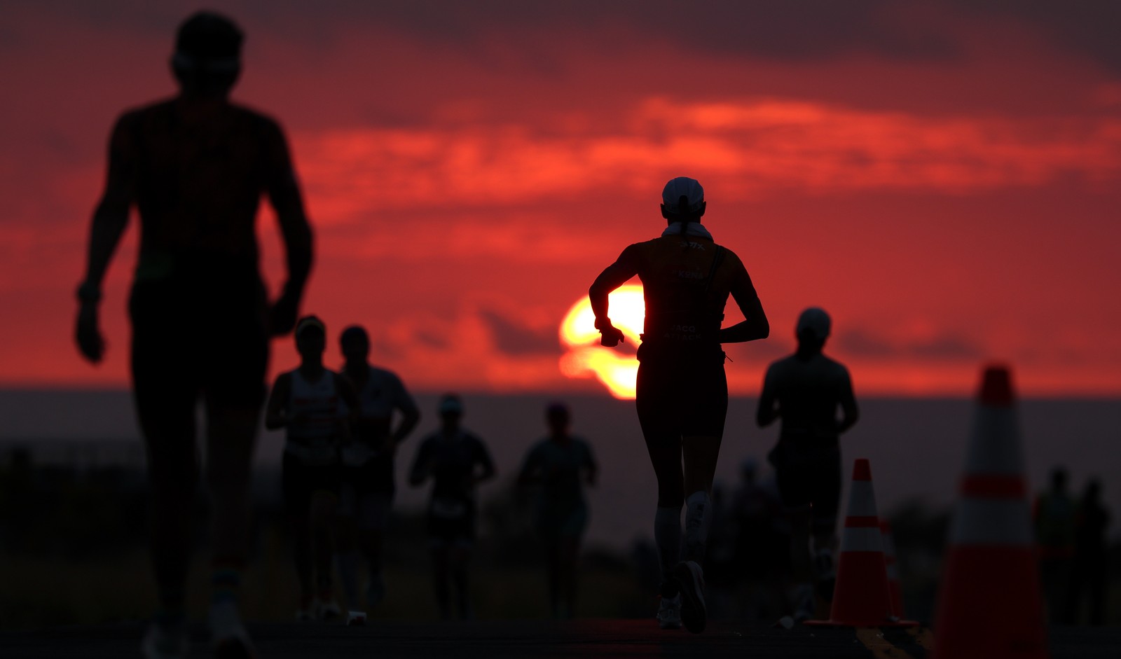 Athletes run in a race, seen silhouetted against a low sun.
