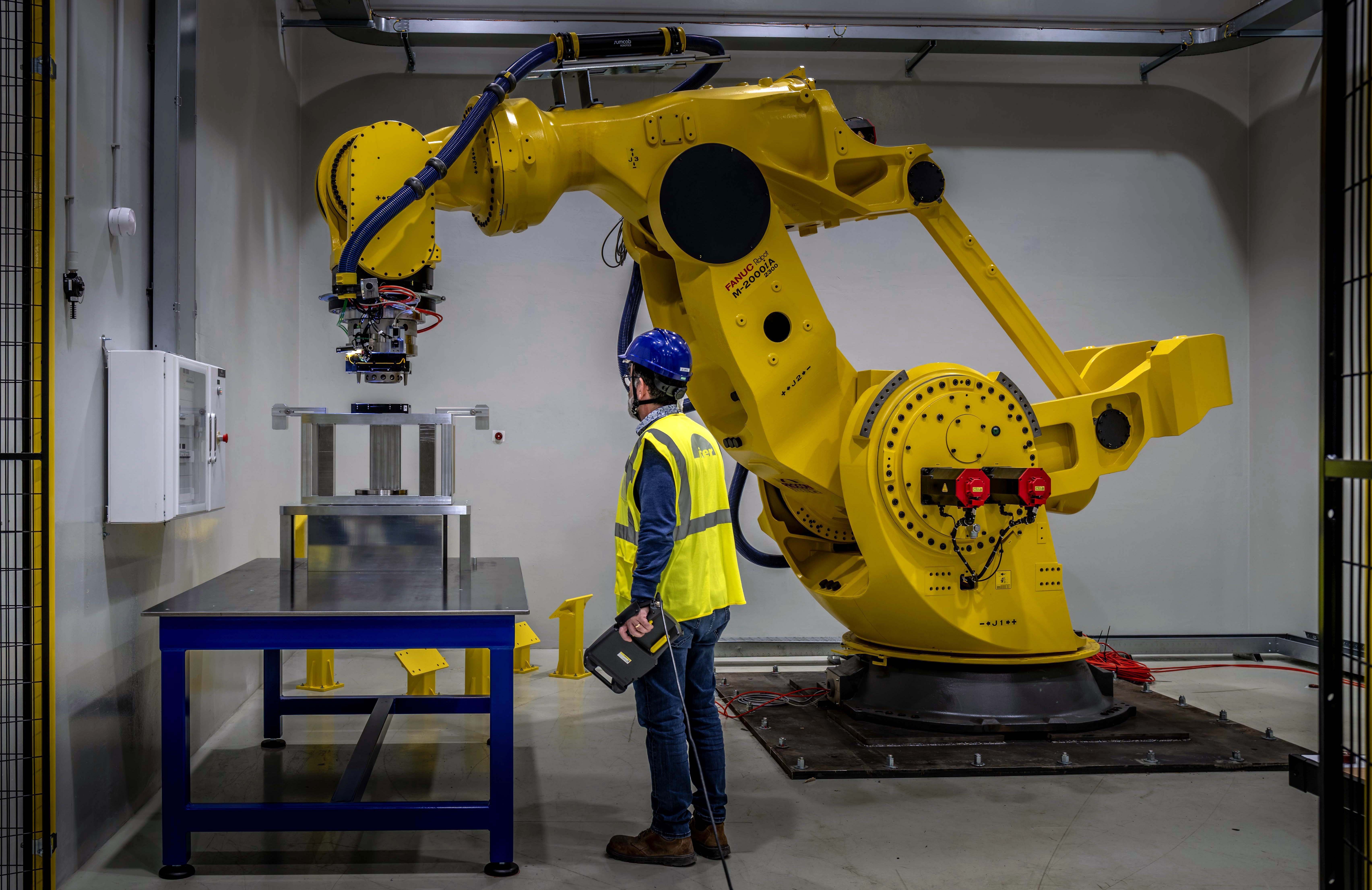 A worker stands beside a tall, massive robotic arm.