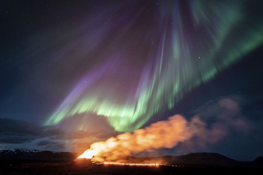 A view of an eruption and lava-flow area, with the northern lights dancing above