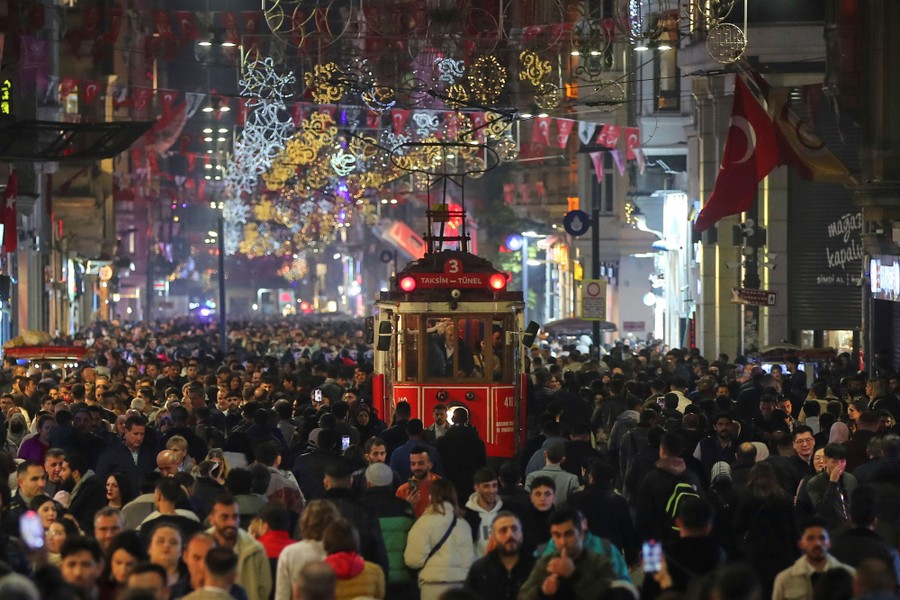 A large crowd of shoppers fills a street, with a tram moving through the middle.