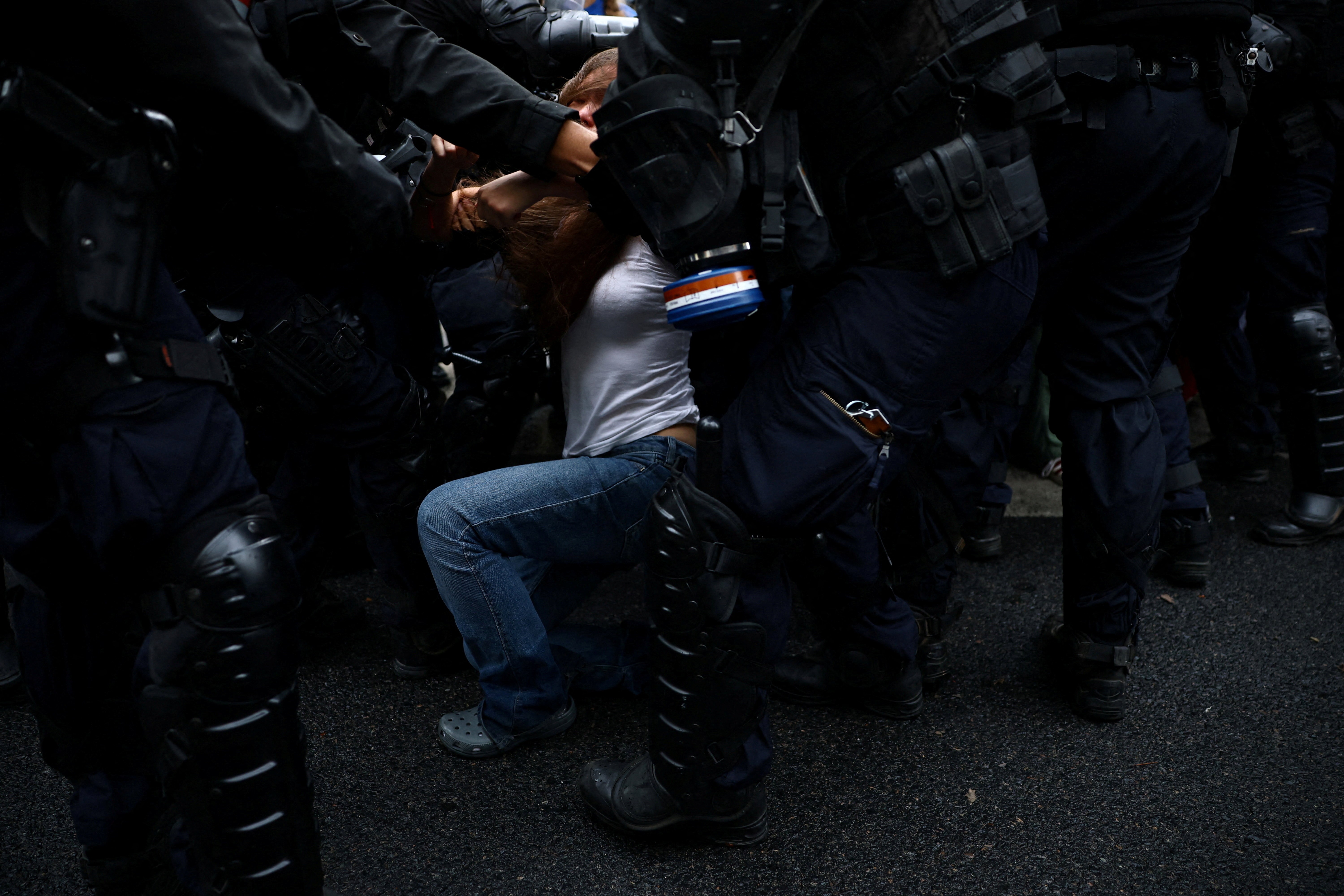 A student protester falls as they are detained by many riot police officers surrounding them.