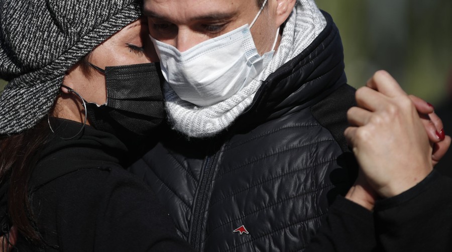 A couple dances close together, wearing jackets, hats, and protective face masks.