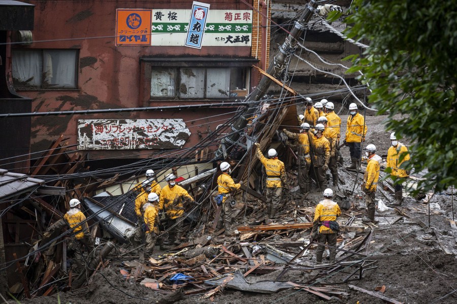 Firefighter work among muddy debris beside a storefront.