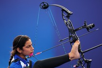 A para-archer draws back an arrow, holding her bow with her right foot.