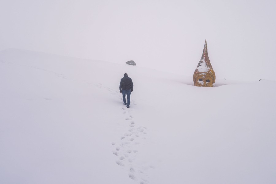 A person walks in snow past the large head of an ancient statue.