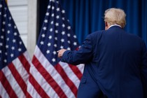 Trump with his back turned, in front of two American flags