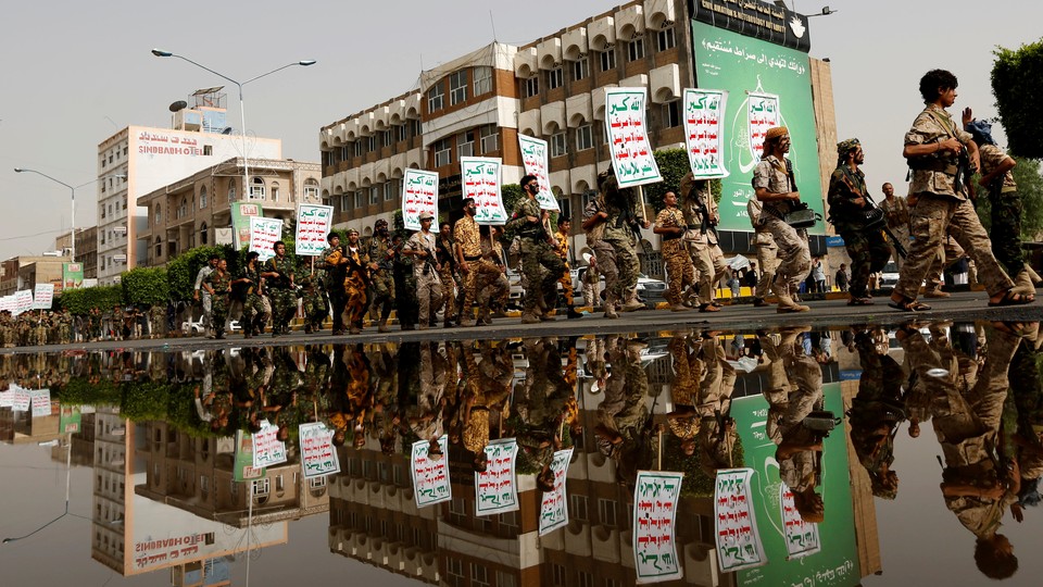 Newly recruited fighters loyal to the Houthi rebels are reflected on a rain water pool as they march with placards reading: "Allah is the greatest. Death to America, death to Israel, a curse on the Jews, victory to Islam". 