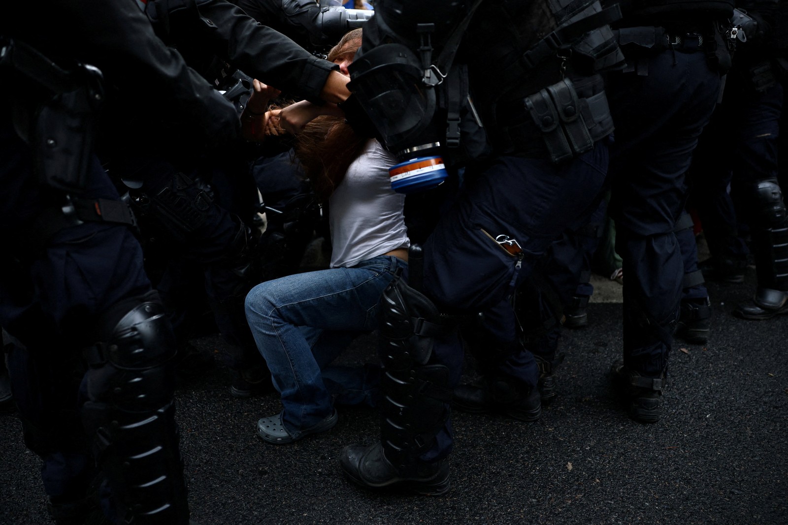 A student protester falls as they are detained by many riot police officers surrounding them.