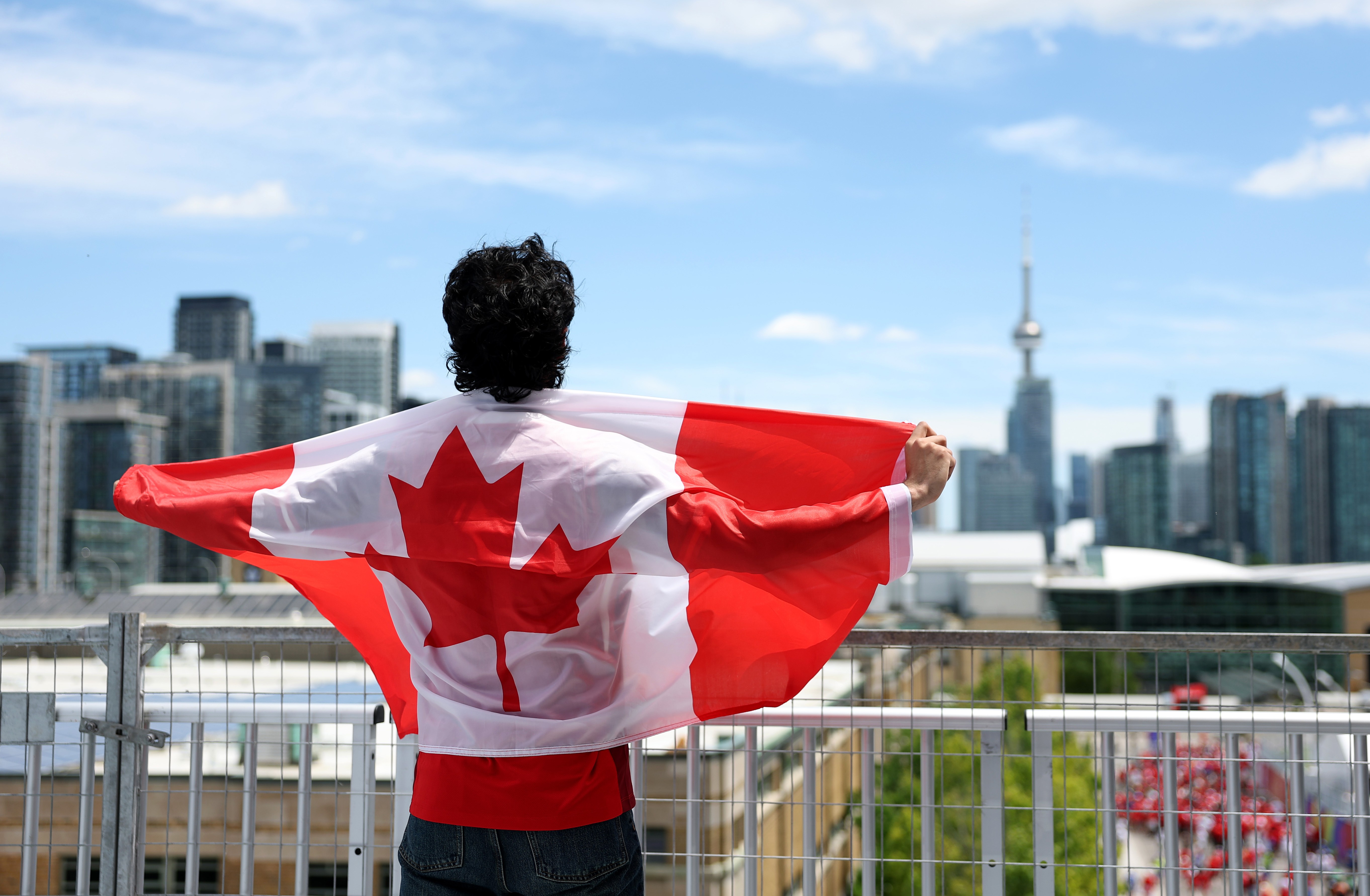 A Team Canada fan, wrapped in a Canadian flag, stands above a stadium with the Toronto skyline in the background.