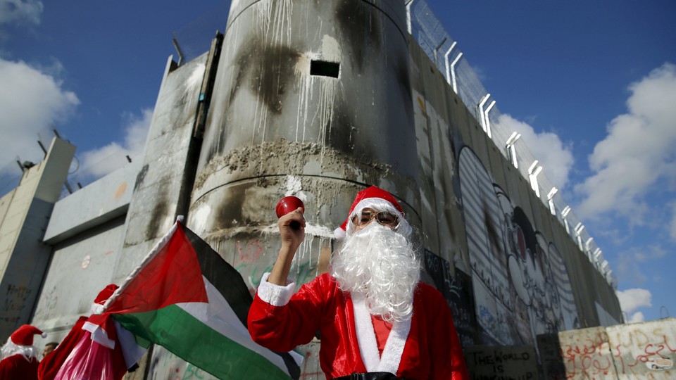 A Palestinian protester wearing Santa Claus costume stands in front of a section of the Israeli barrier during an anti-Israel protest in the city of Bethlehem on December 18, 2015. 