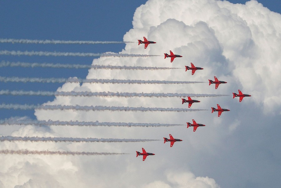 Ten red jets fly in formation in front of a large cloud.