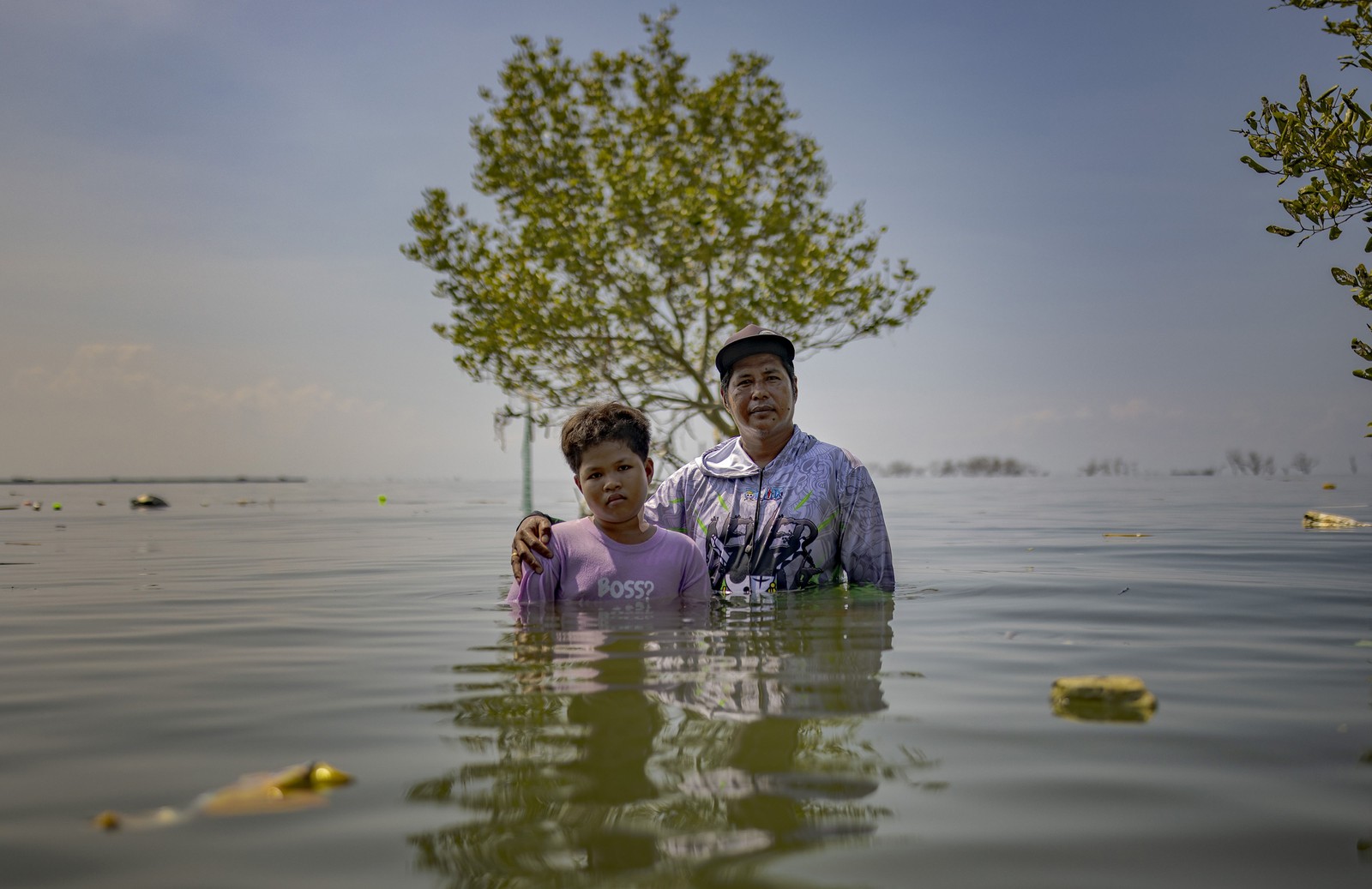A man and a boy stand side-by-side in chest-deep floodwater.