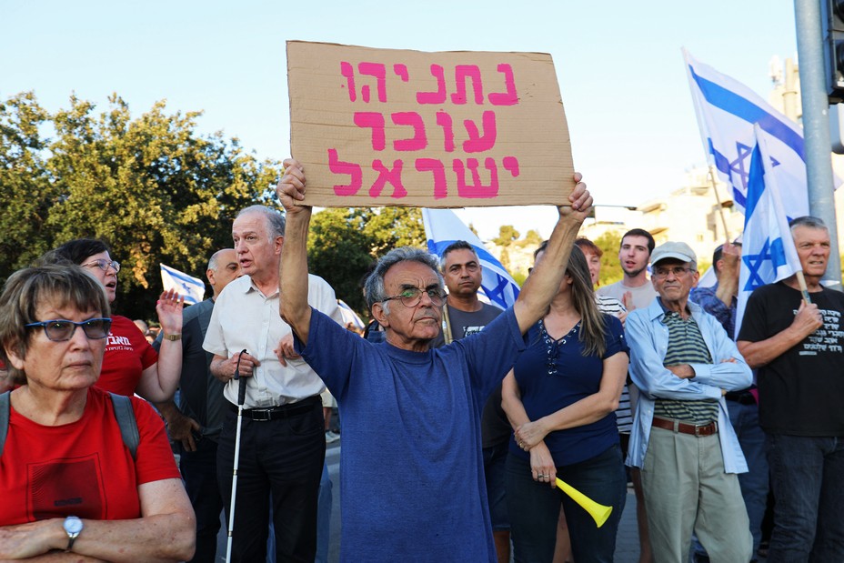 A protester holds a sign in Hebrew that says "Netanyahu is the troubler of Israel"