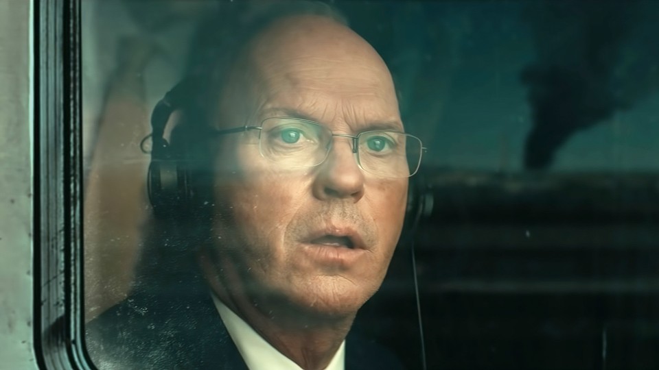 A man looks out of a train window at smoke rising in the distance