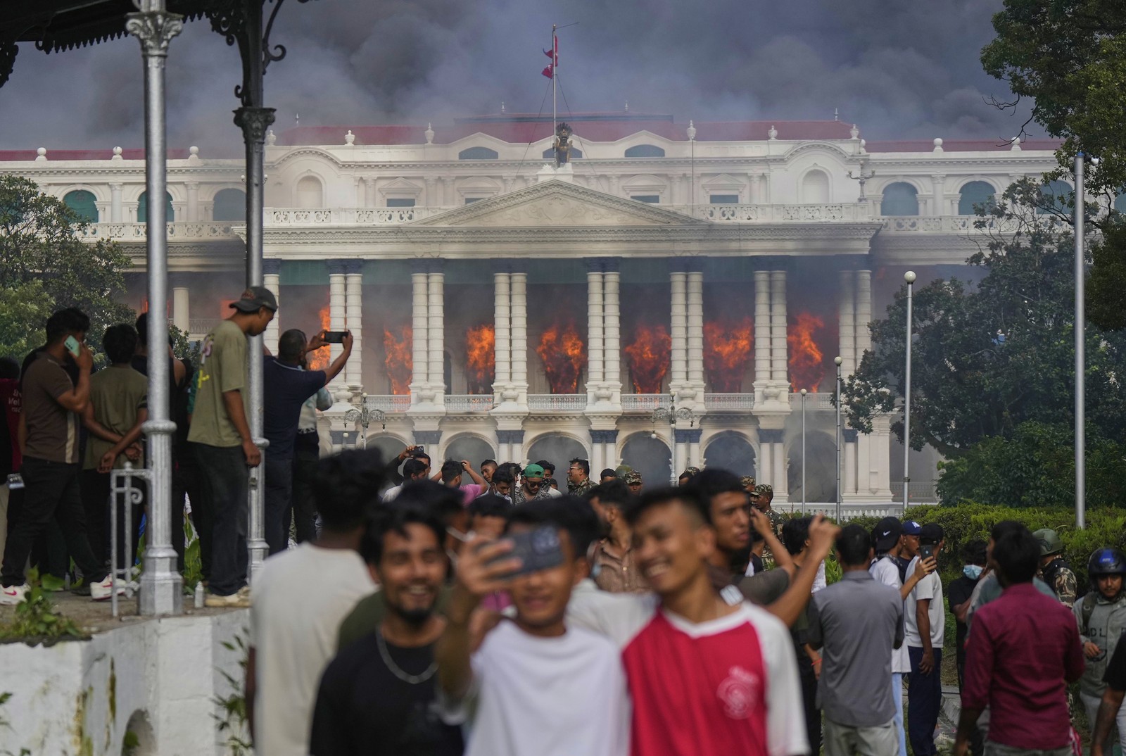 Many demonstrators mill about, while some take selfies, in front of a burning government building.
