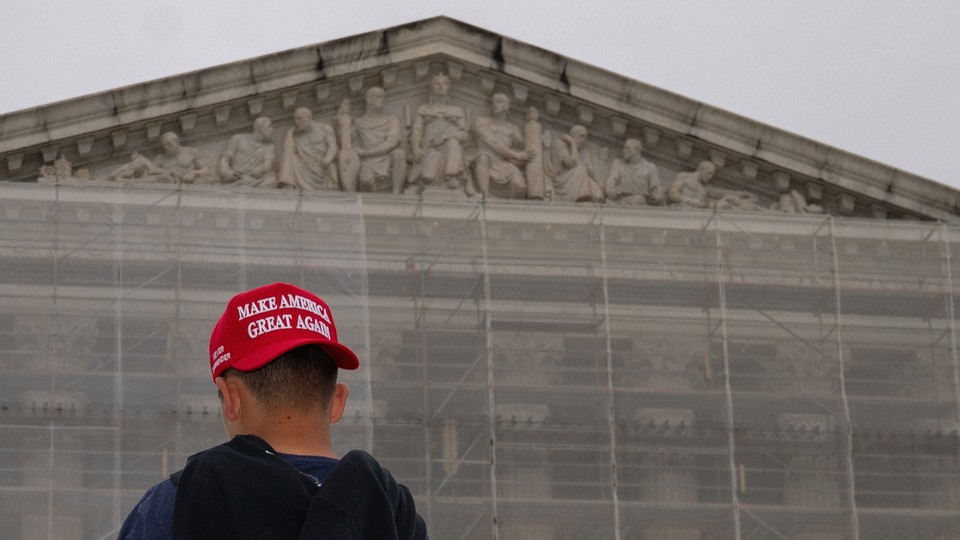 Photograph of a boy wearing a backwards “Make America Great Again” cap in front of the Supreme Court building with scaffolding