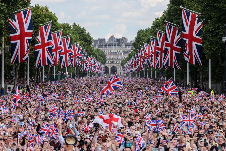 An open pathway is filled with thousands of people waving British flags.