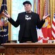 Elon Musk stands next to a seated Donald Trump.