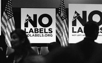 A conference room full of people, American flags, and signs that say "No Labels"