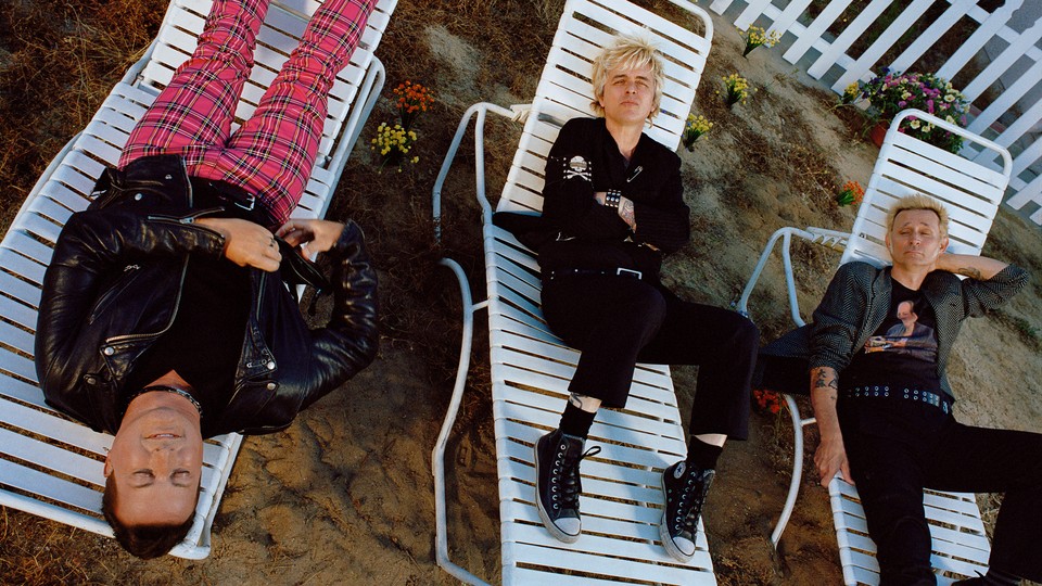 the three members of green day lying on white lawn chairs