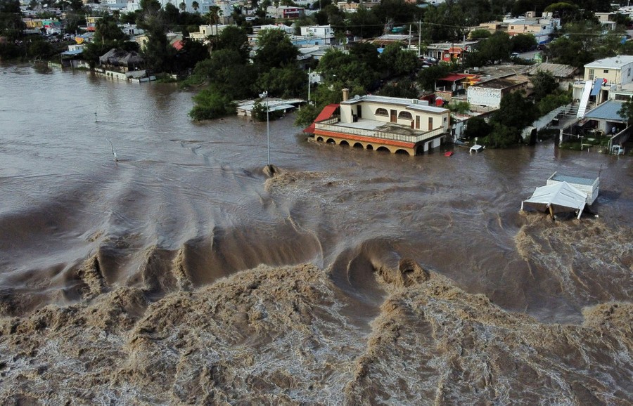 An aerial view of fast-moving floodwater passing by and through a neighborhood