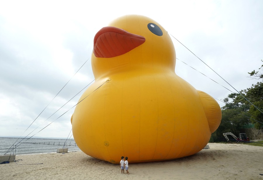 Two young children stand beside an enormous inflatable rubber duck.
