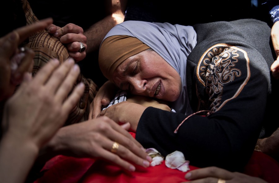 A despondent woman leans over the body of her son, among other mourners.