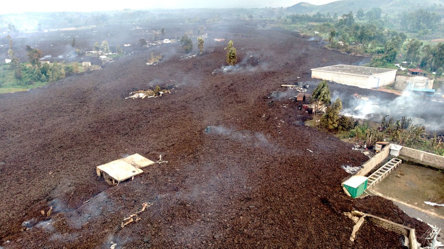 Steaming volcanic rock surrounds buildings, seen from above.