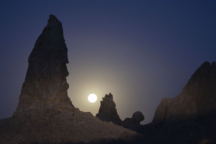 The full moon beyond rough natural pinnacles in a desert.